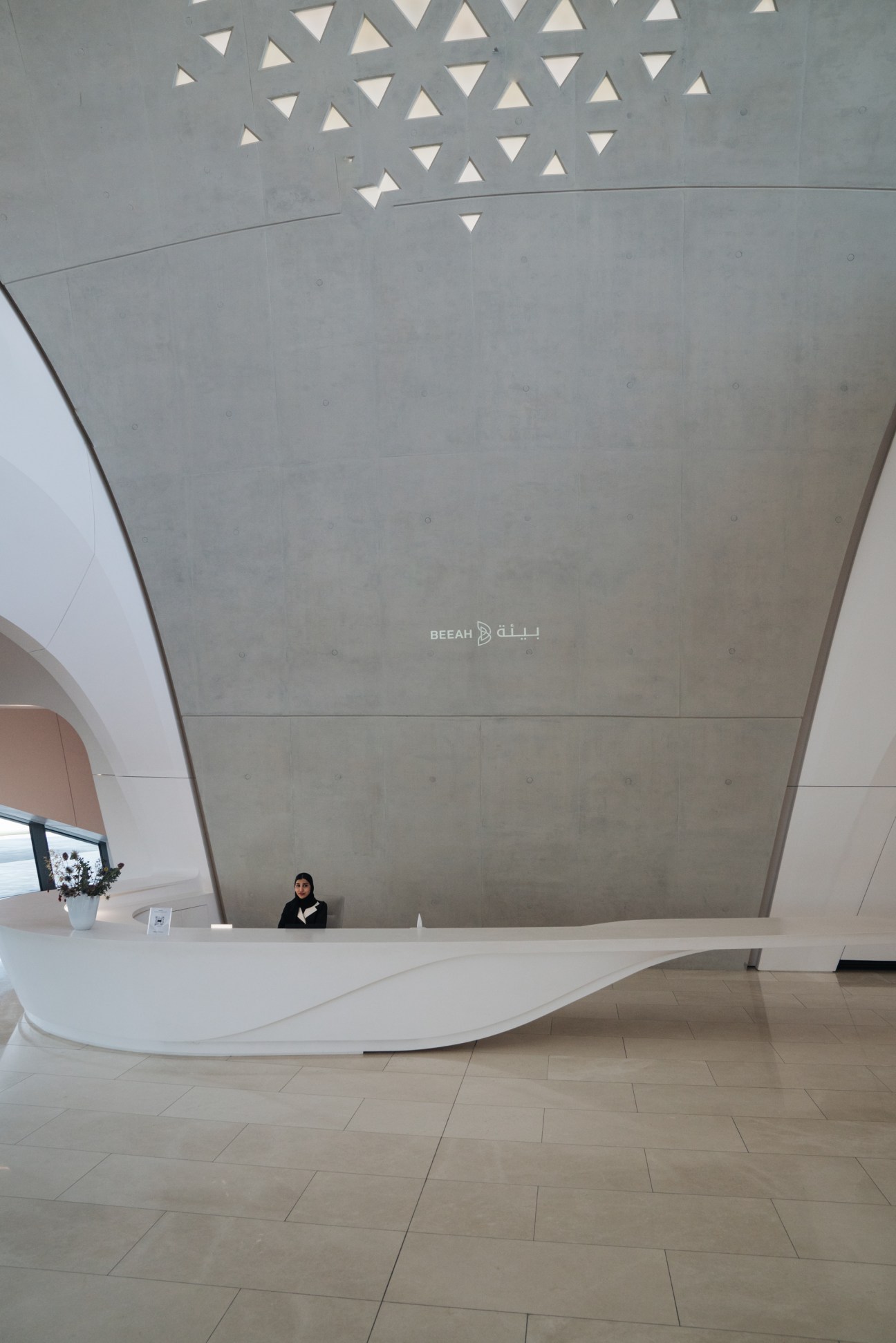 Beeah HQ reception desk with curved concrete ceiling and triangular skylights filtering sunlight.