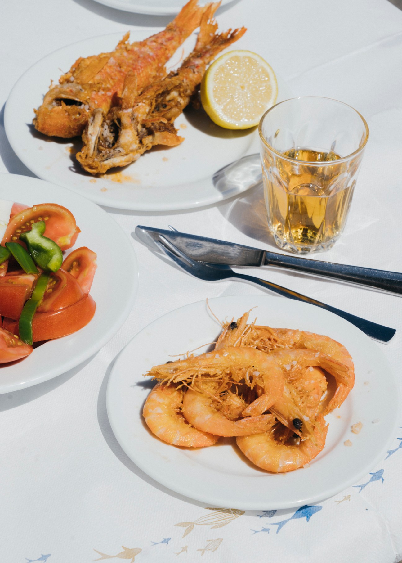 Fried seafood platter with shrimp and fish, lemon wedge, salad, and glass of white wine on white plates