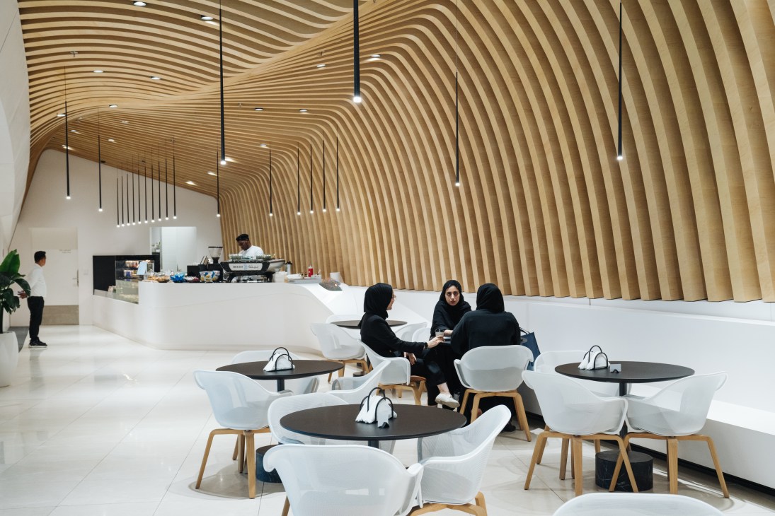 Beeah HQ canteen with rippling wooden ceiling, white chairs, black tables and staff dining.