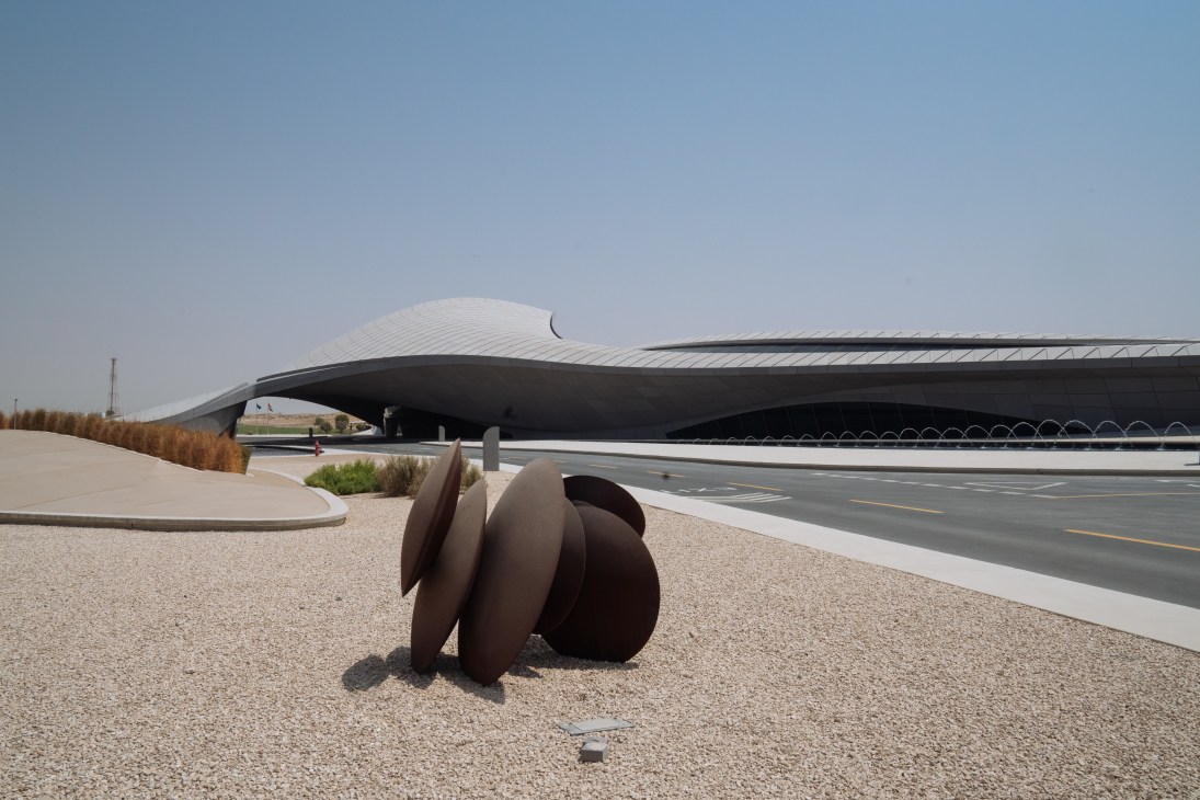Beeah HQ's undulating curved structure and sculptural landscaping viewed from the desert grounds alongside a highway.