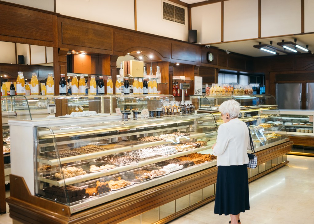 Customer browsing pastries in the display cases at Asimakopouloi bakery in Athens.