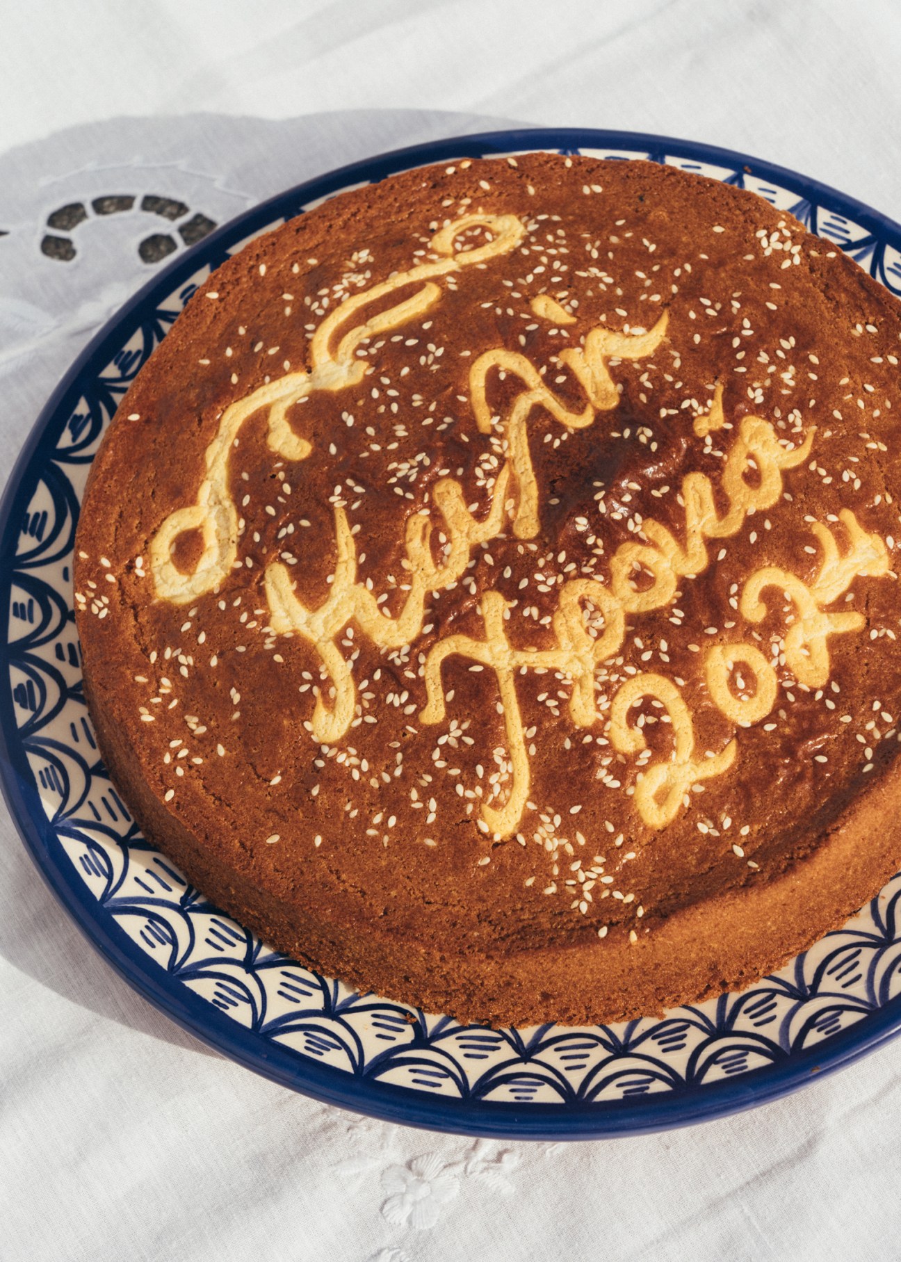 Vasilopita Greek New Year's cake on decorative blue and white plate with sesame seeds and piped design.