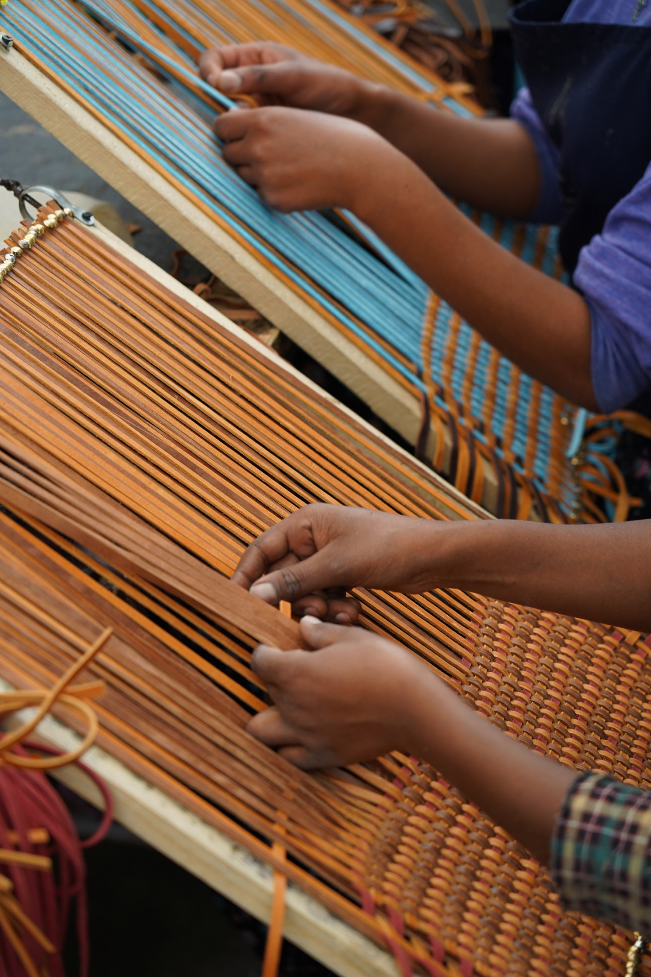 Hands working on traditional weaving with golden and blue threads at Sabegn workshop in Addis Ababa.