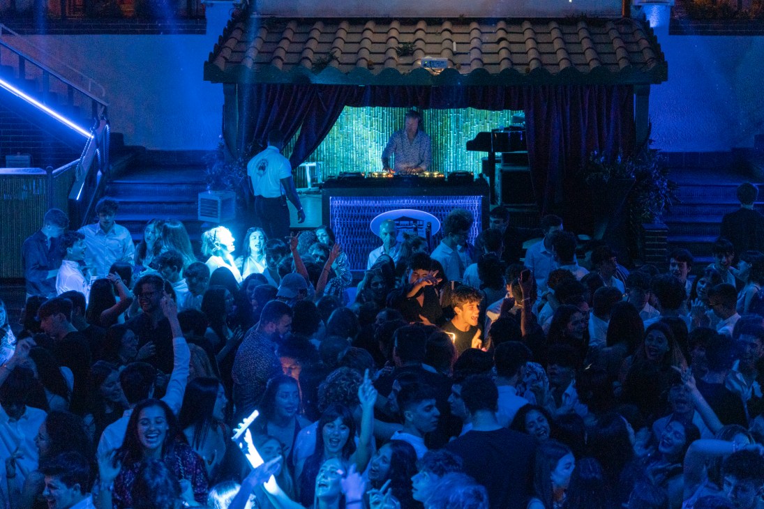 Crowded nightclub scene with people dancing under blue lighting and DJ booth with decorative roof structure