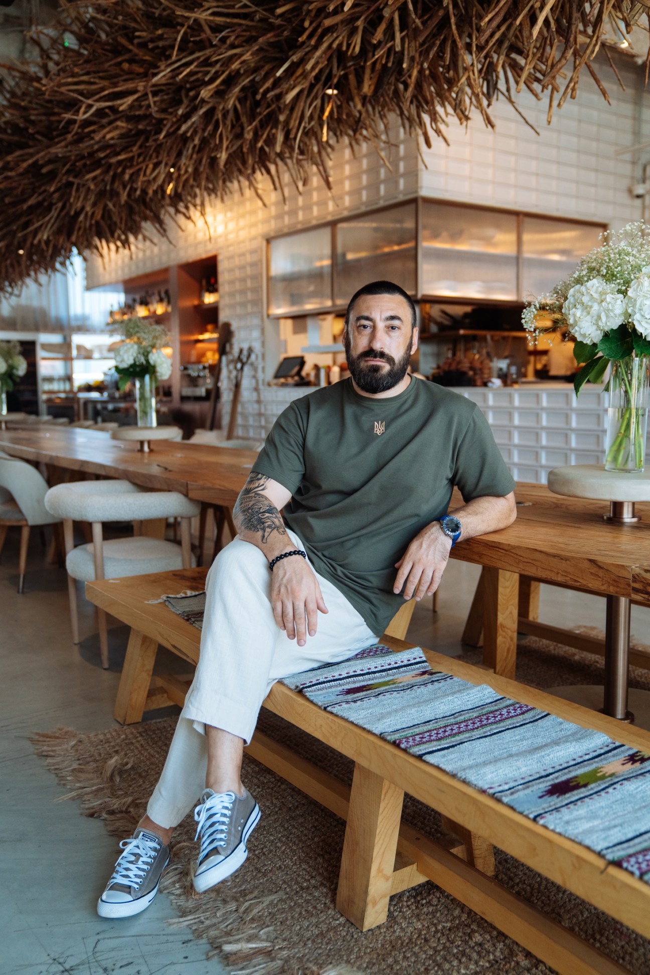Man sitting on wooden bench in modern restaurant with palm frond ceiling.