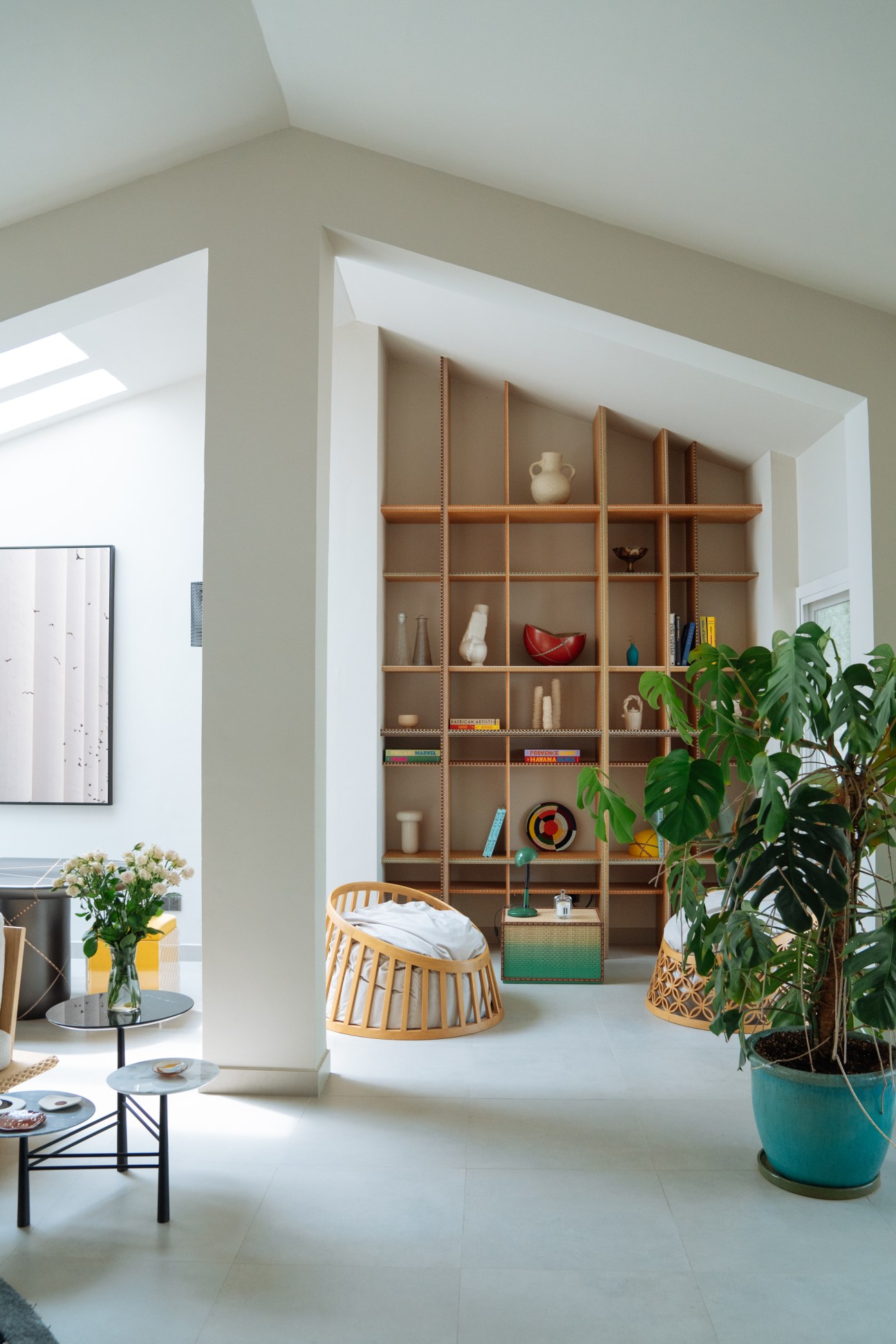 Minimalist interior with wooden shelving unit, woven chair, potted plant and curated objects in natural light.