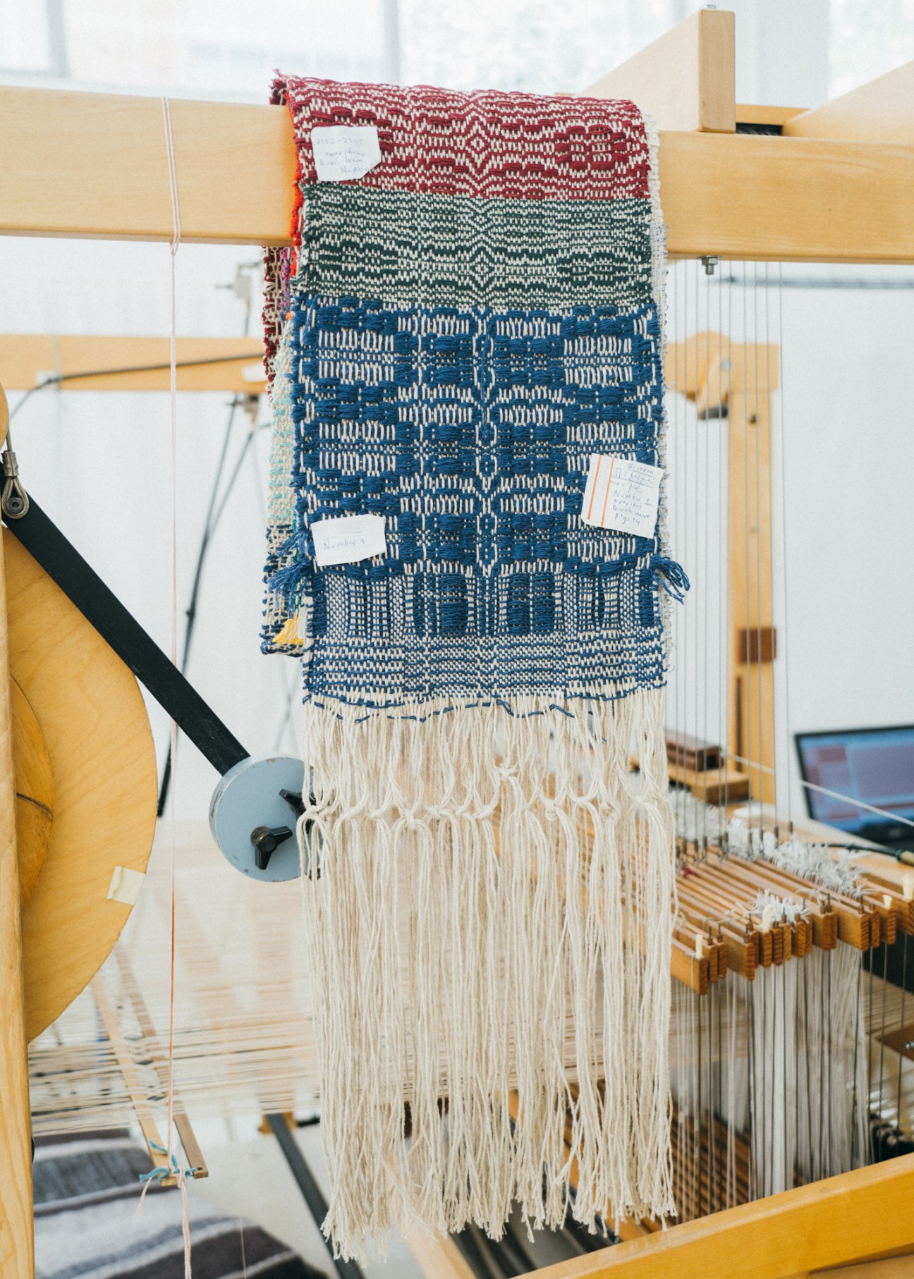 Traditional textile samples with geometric patterns in red, green, and blue hanging on wooden loom