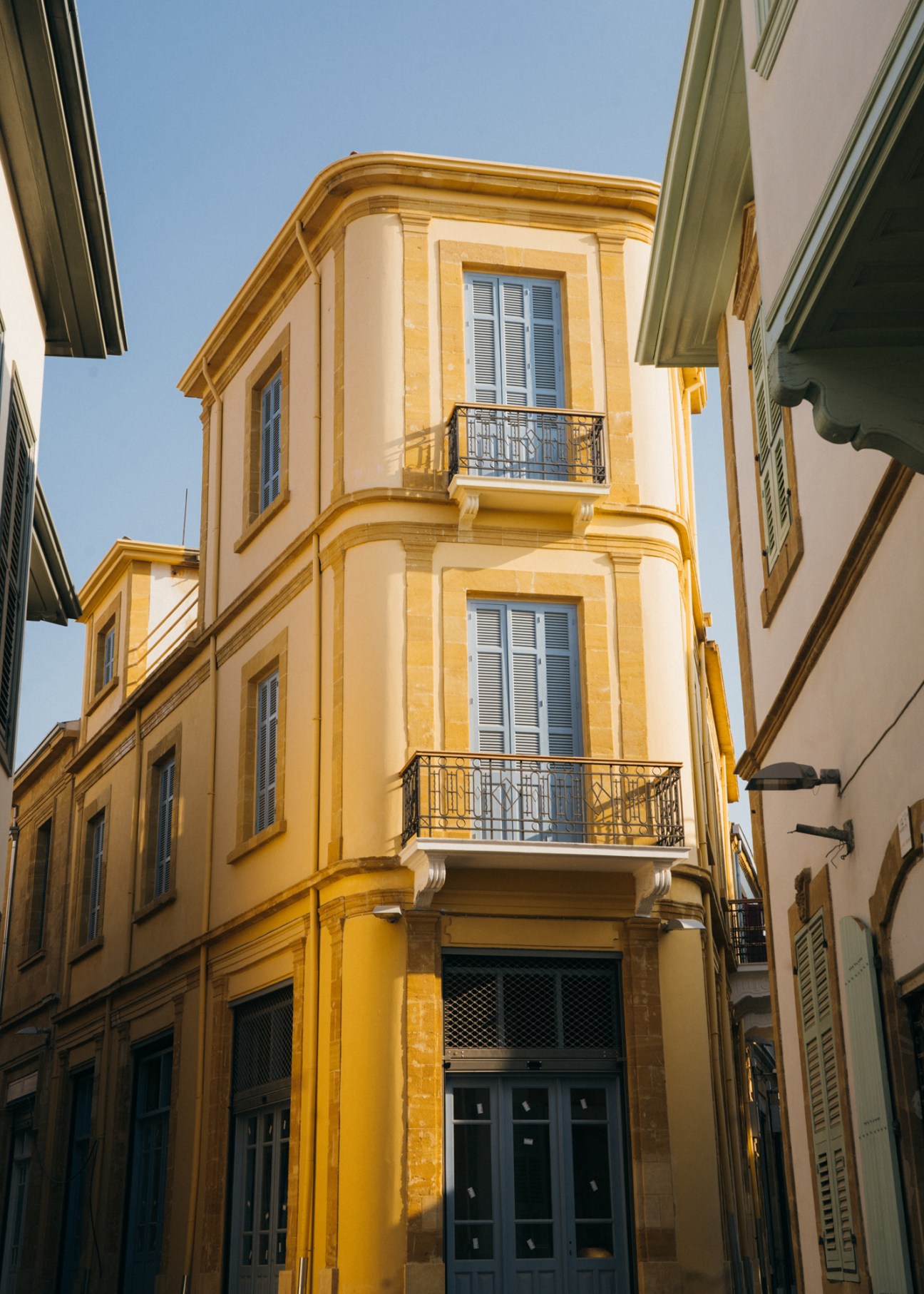 Golden neoclassical corner building with curved facade, blue shutters and ornate balconies in old Nicosia