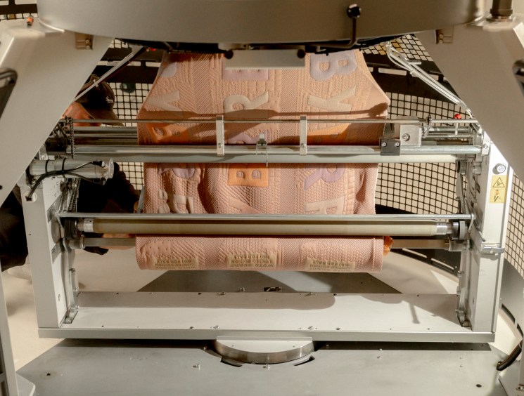 Close-up view inside an industrial knitting machine showing the mechanical components and yarn threading