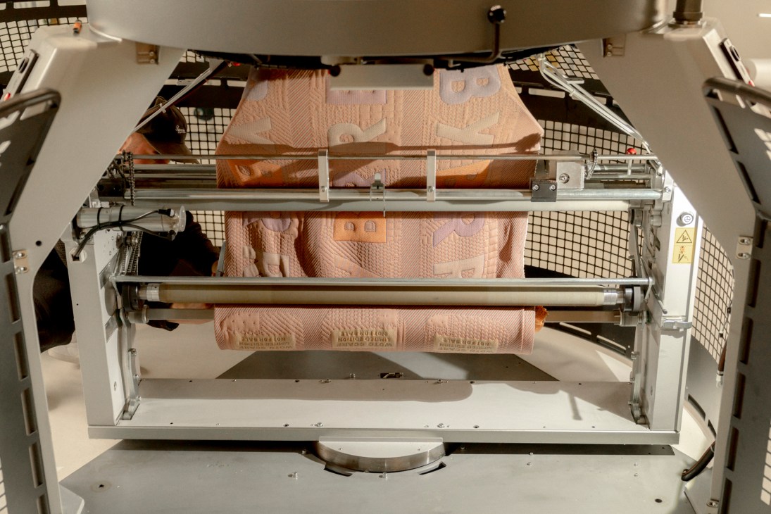 Close-up view inside an industrial knitting machine showing the mechanical components and yarn threading