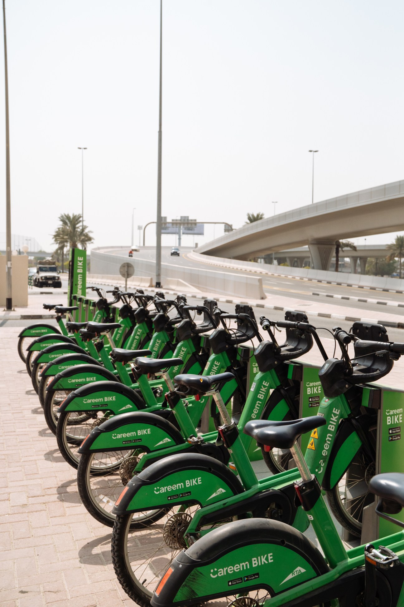 Green Careem Bike bicycles lined up at a docking station in Dubai's Media City, with an elevated highway in the background.