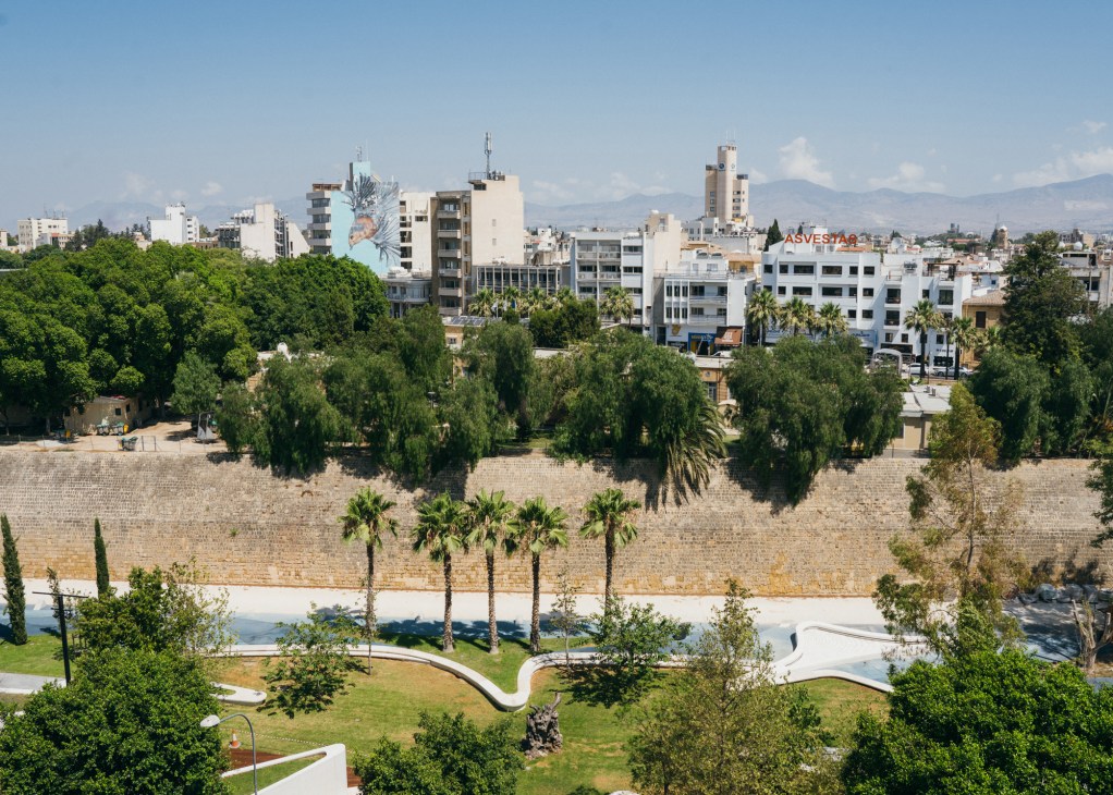 Aerial view of Nicosia showing historic stone walls, palm trees, modern buildings and mountains in background