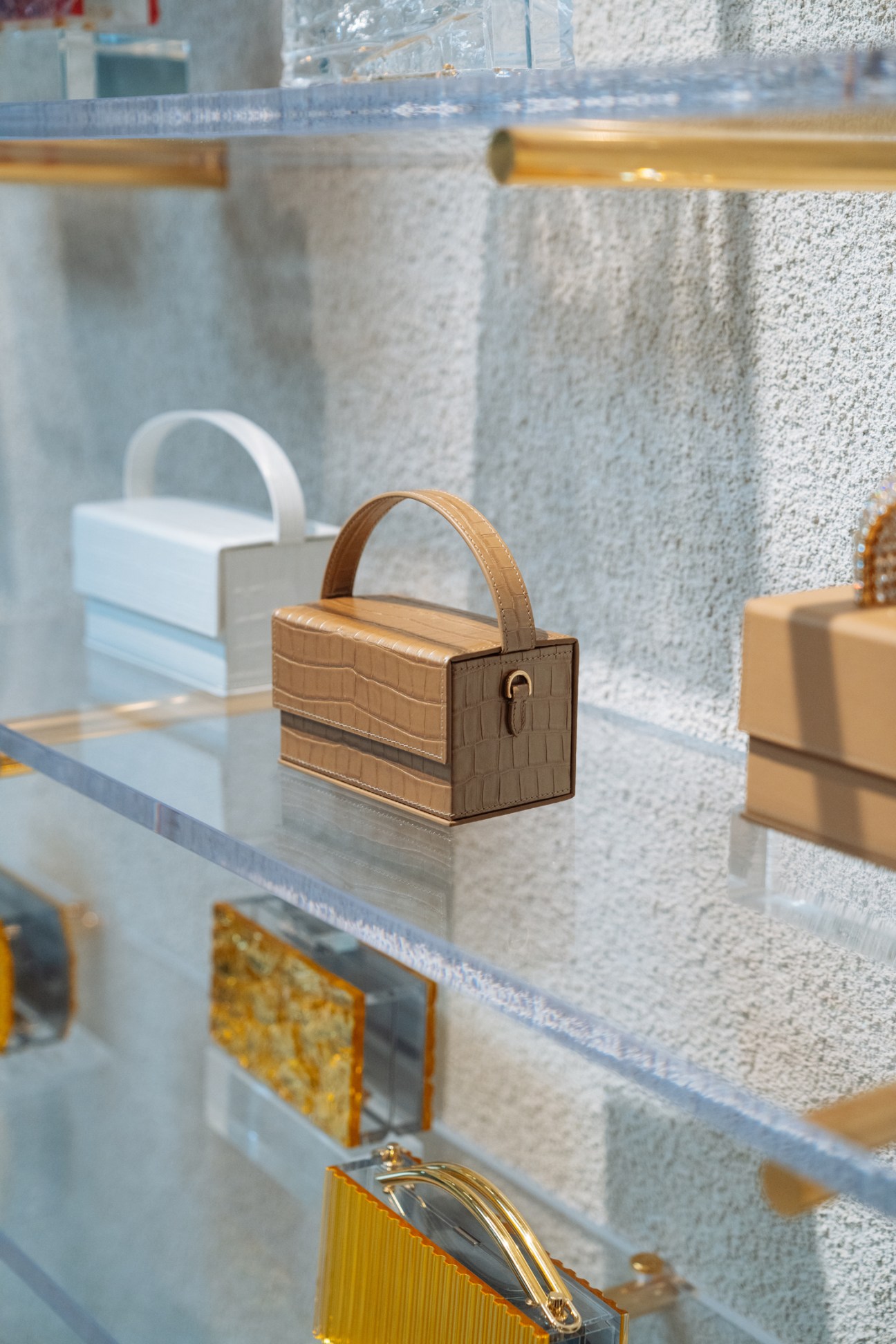 L'Afshar crocodile-textured leather handbag with handle displayed on glass shelf in studio.