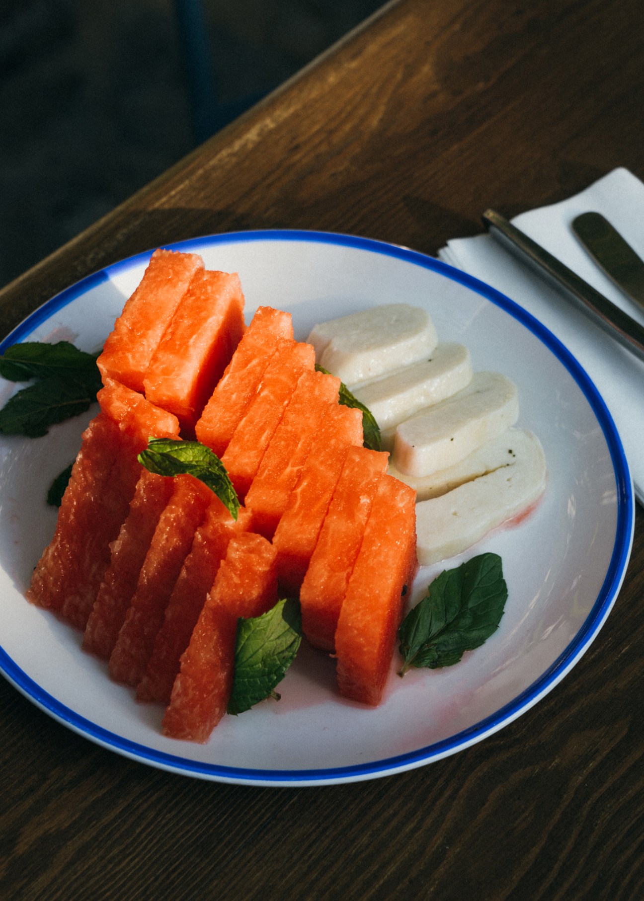 Sliced watermelon and white cheese arranged on a white plate with mint leaves