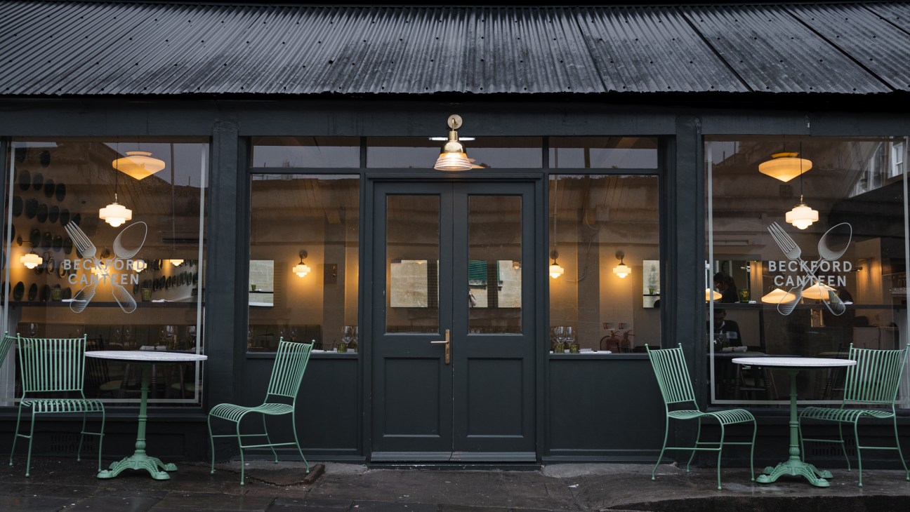 Beckford Canteen storefront with dark windows, green metal chairs, brass pendant lights, and corrugated metal roof.
