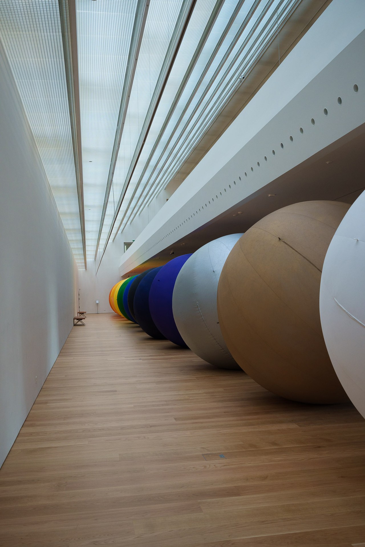 Large colorful inflatable spheres displayed in a gallery space with skylights.