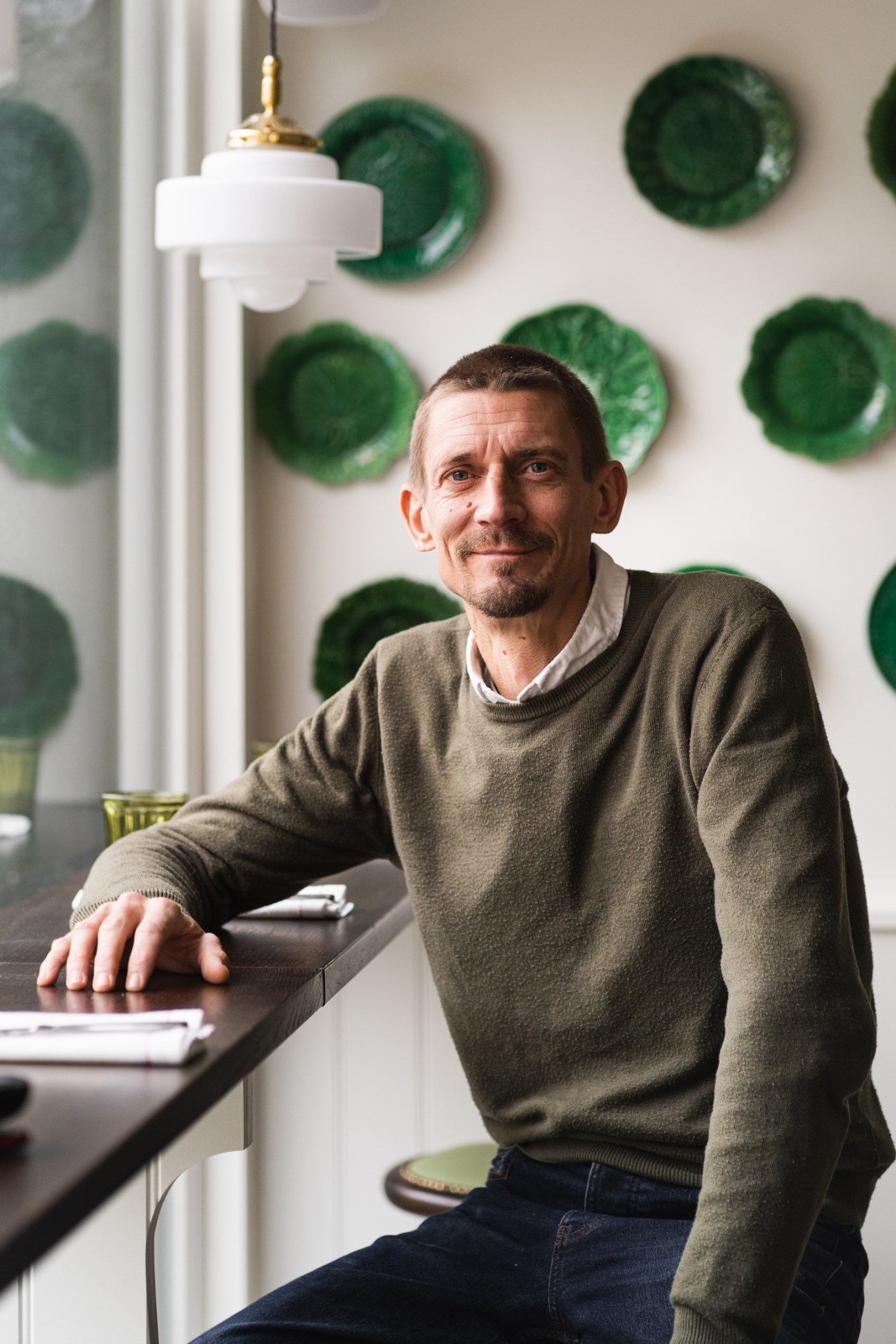 Operations director Ollie Sutton seated at a table in Beckford Canteen with green decorative plates on the wall behind him.
