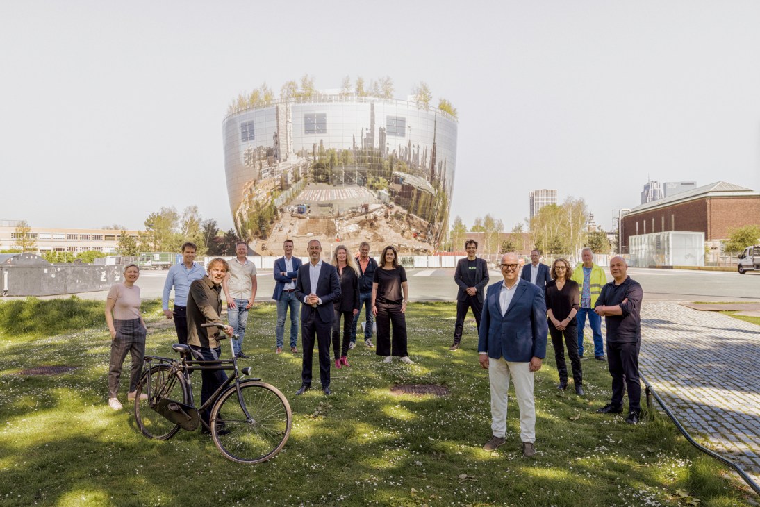 Team of architects, engineers and museum directors stand on grass before Rotterdam's cylindrical Boijmans art depot building.