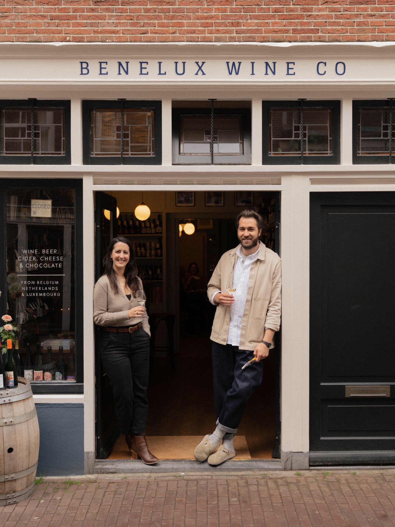 Two people standing in the doorway of Benelux Wine Co holding wine glasses