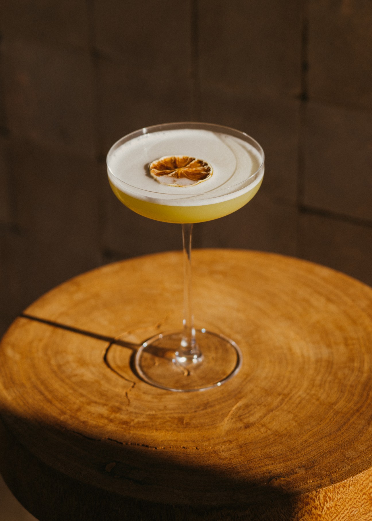 Cocktail with white foam topping and dried orange slice garnish on wooden surface