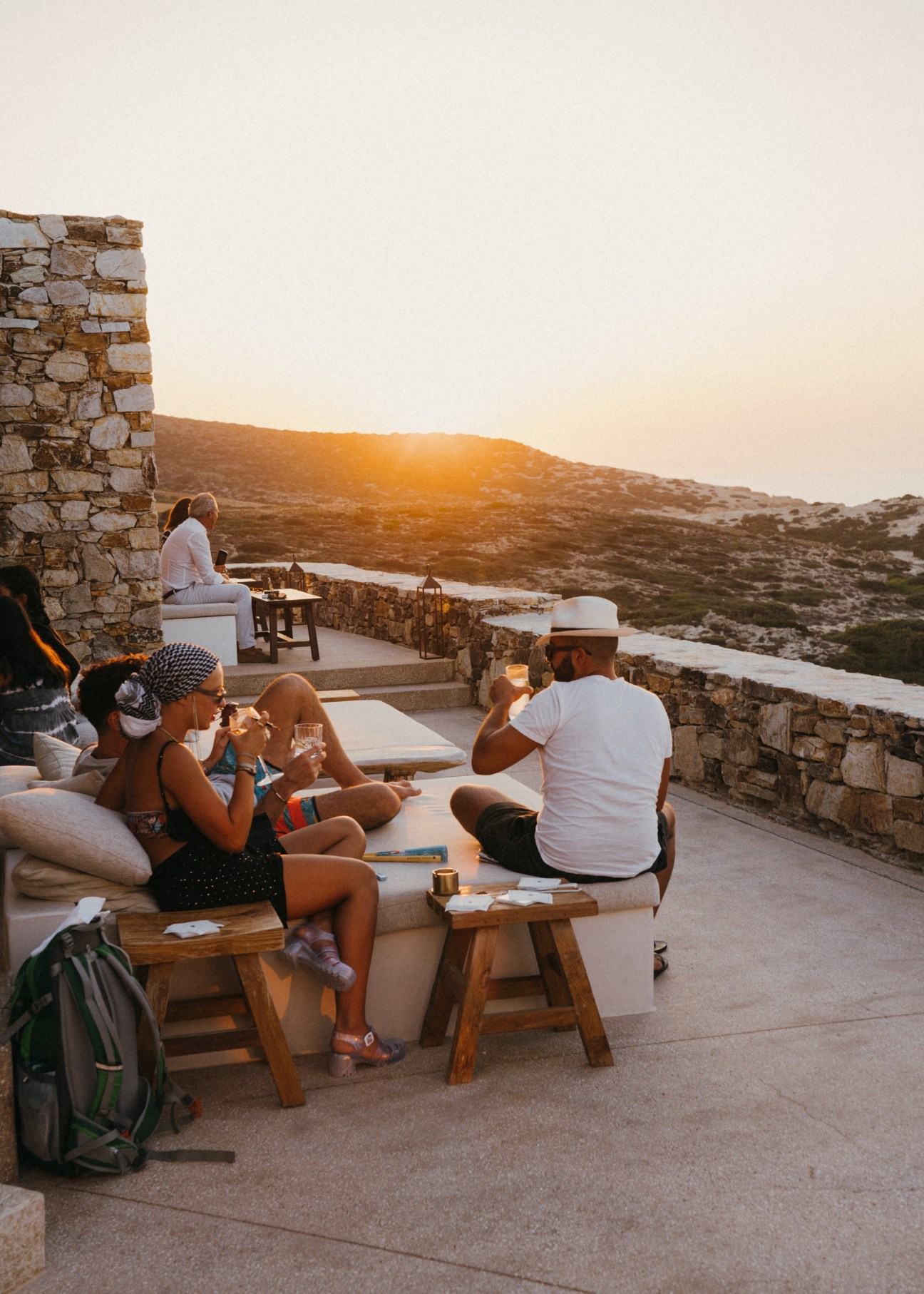 Guests relaxing on terrace seating with drinks at sunset overlooking hills and coastline