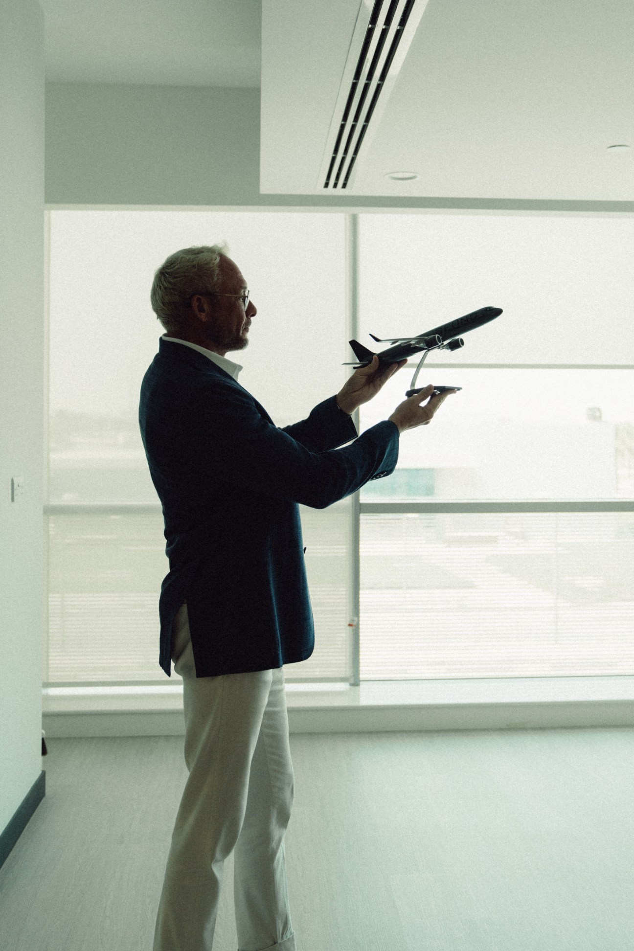 Man in business attire holding aircraft models by a window in a modern office