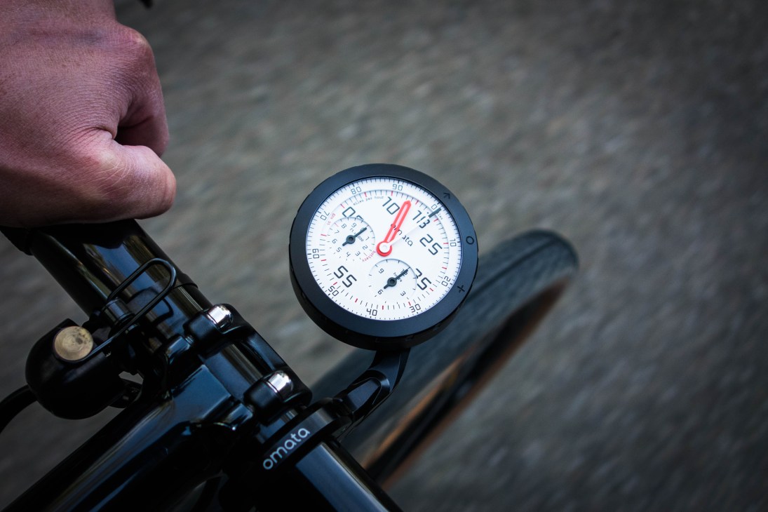 Close-up of Omata bicycle speedometer showing analog-style gauge with white face and red needle