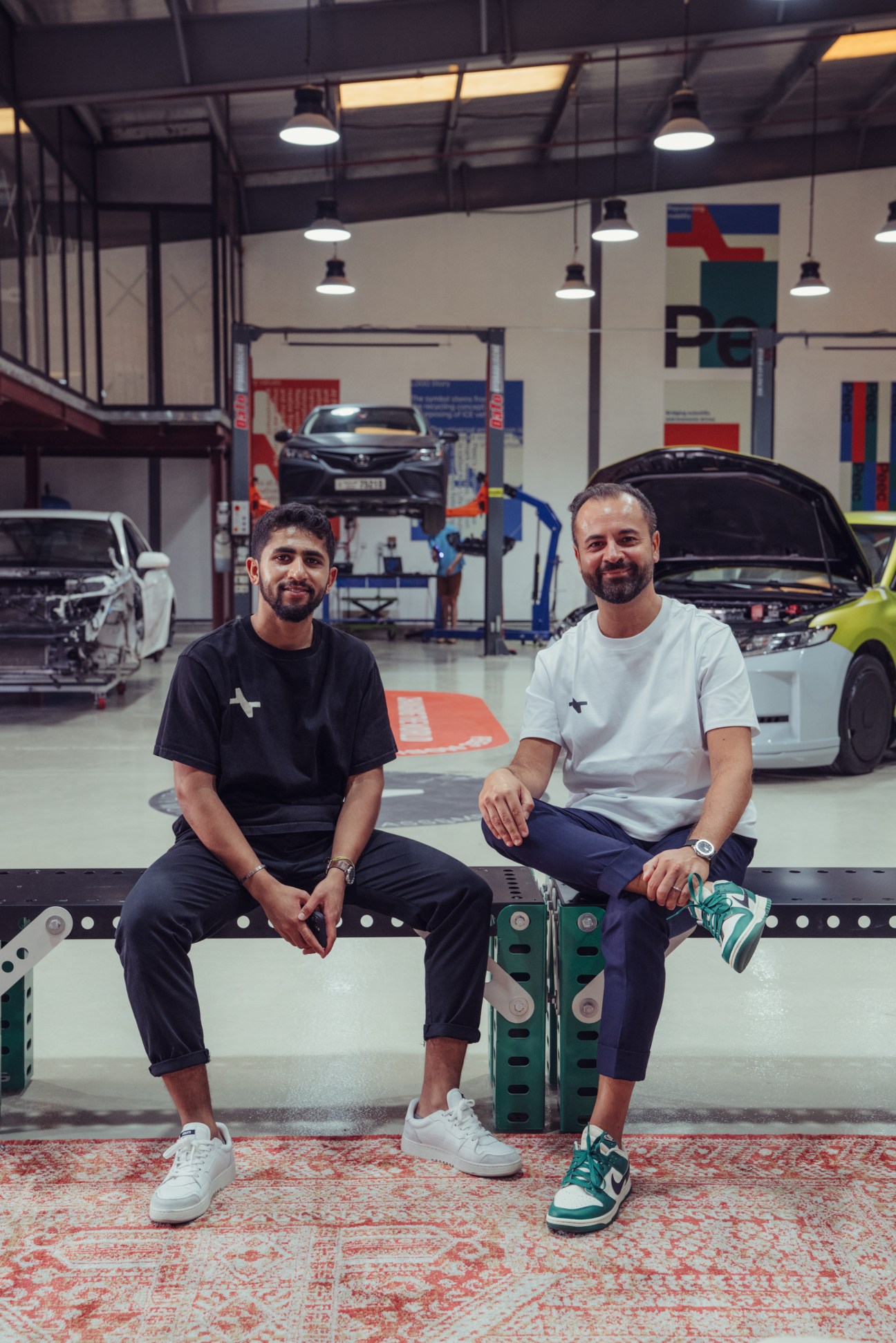 Founder Zach Faizal and head of partnerships Luca Cappuccitti sitting in Peec's workshop surrounded by electric vehicle conversions.