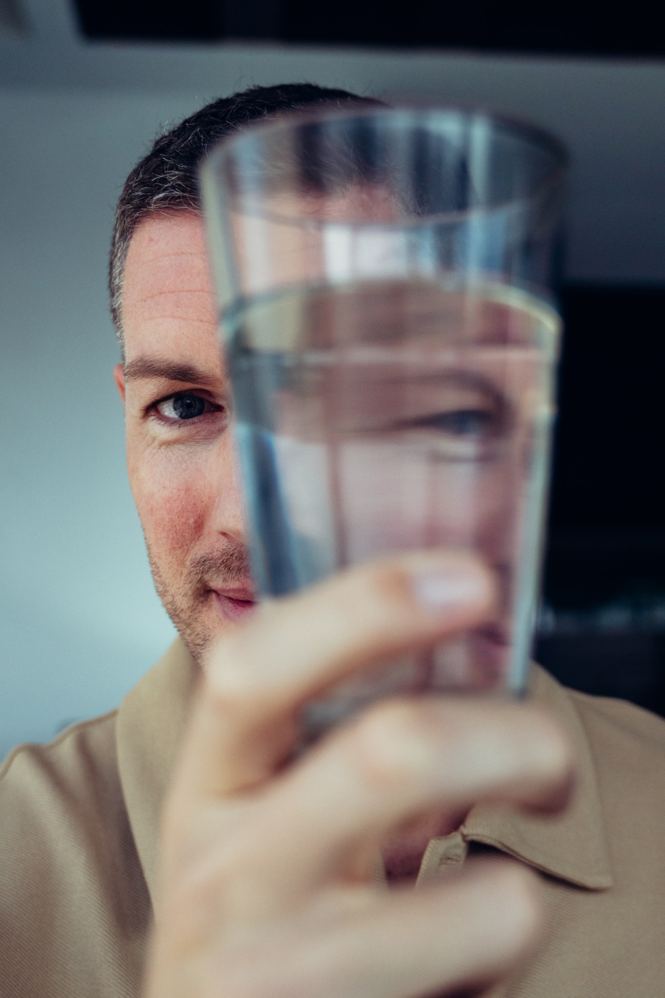 Man holding a glass of water in front of his face.