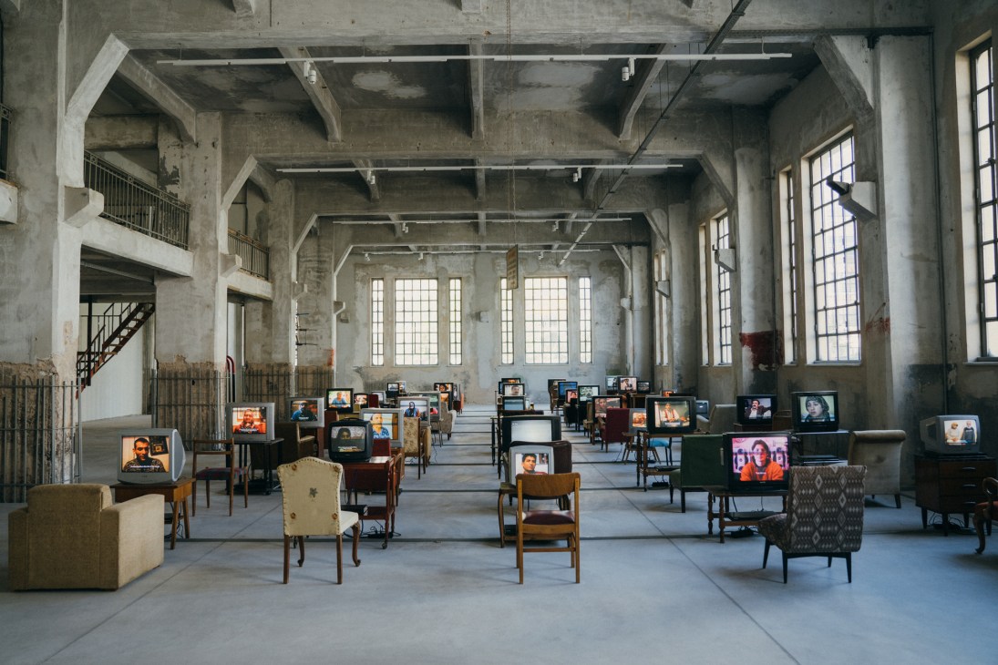 Installation view of 'Küba' by Kutlug Ataman showing vintage televisions and chairs in a concrete industrial space.