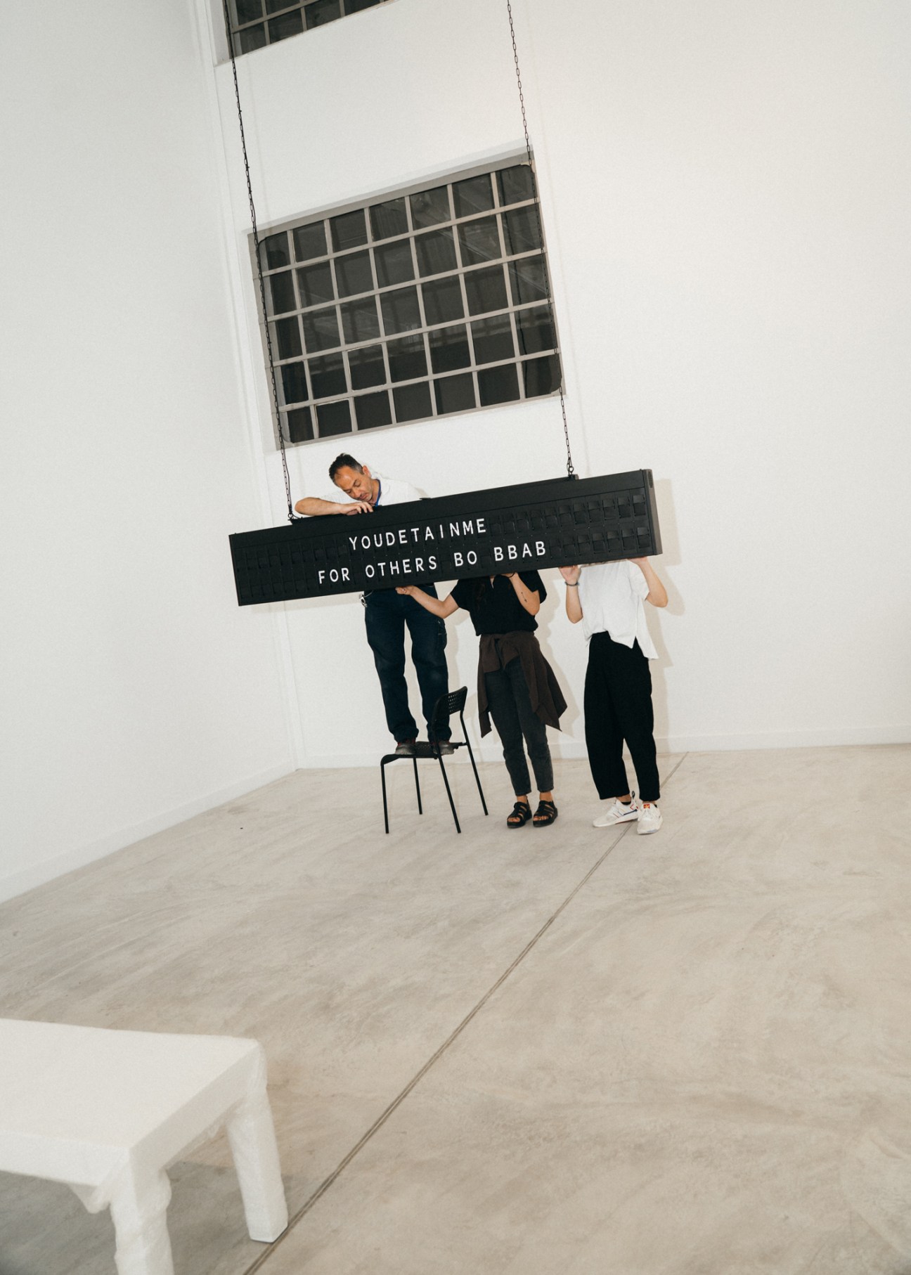 Visitors interact with Shilpa Gupta's airport-style installation featuring rotating characters and words displayed on a suspended black panel.
