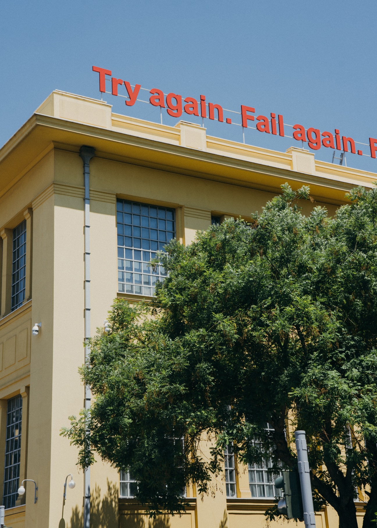 Red neon text reading 'Try again. Fail again.' on a cream-colored building facade with ivy.