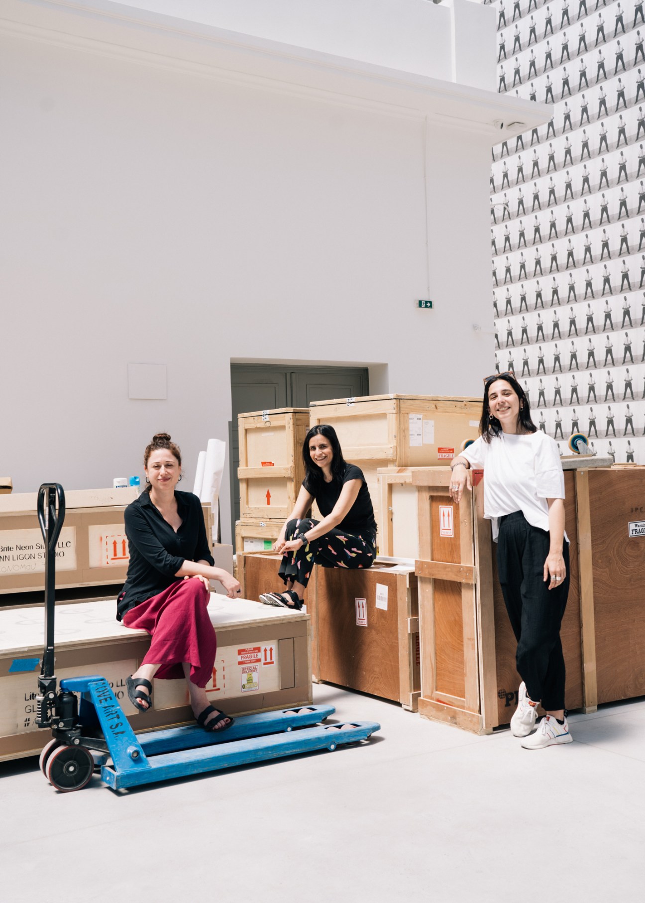 Neon director Elina Kountouri and two staff members pose among wooden crates in a gallery space during installation.