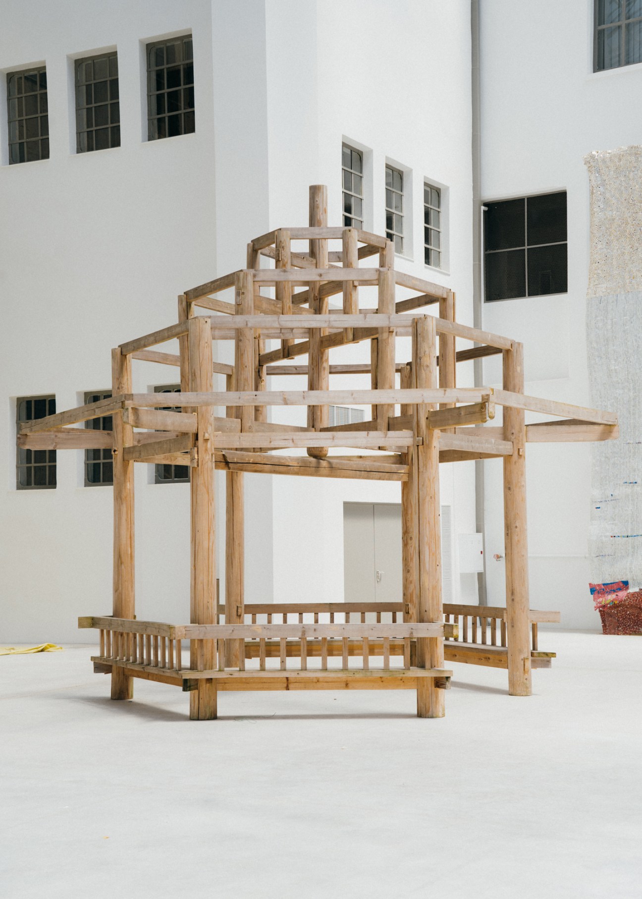 Wooden pavilion structure with tiered platform and railings by Vietnamese artist Danh Võ in gallery space.