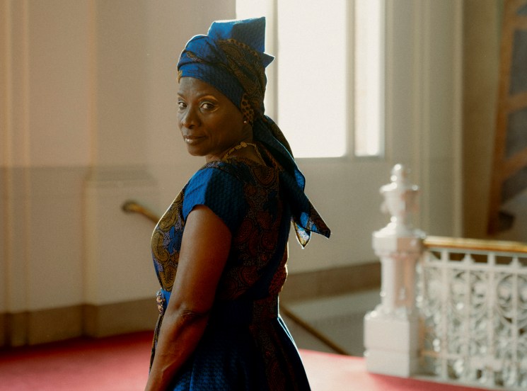 Woman in vibrant blue patterned African dress with matching head wrap standing in elegant interior space
