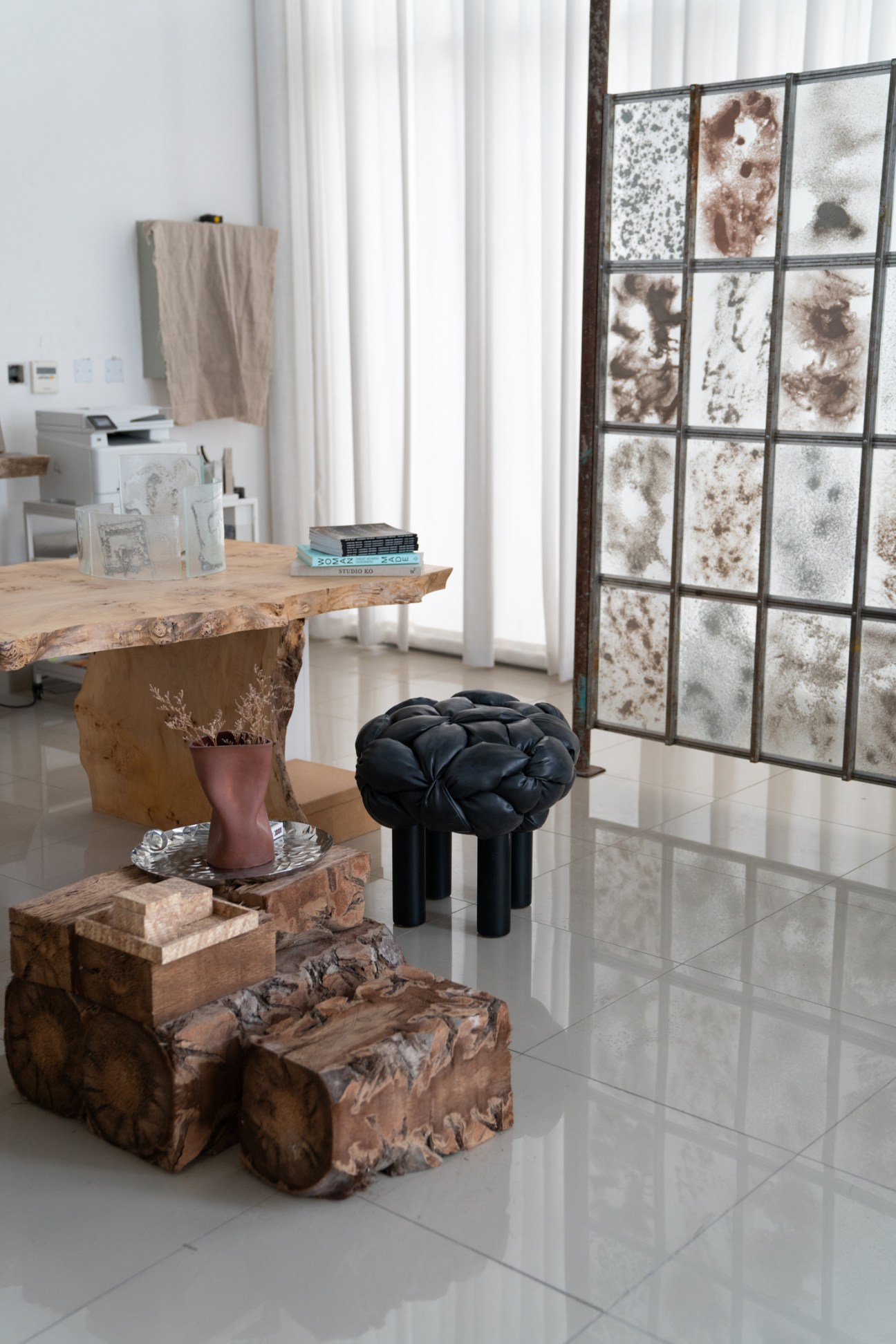 Artist Latifa Saeed's studio displaying wood furniture pieces, sand samples in a grid display, and ceramic vessels in neutral tones.