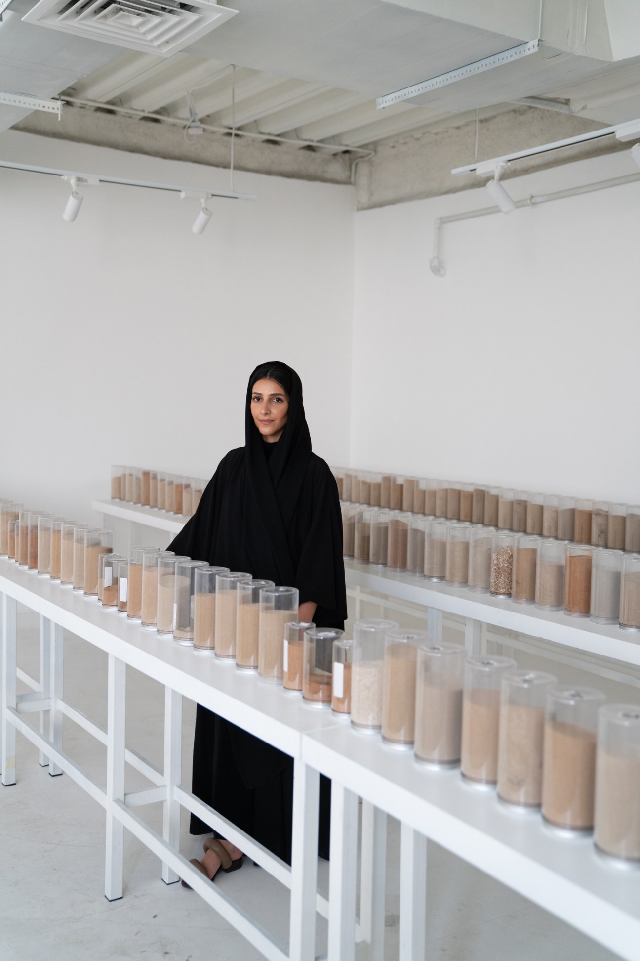 Latifa Saeed stands in her Dubai studio surrounded by over 250 containers of sand collected from across the UAE.