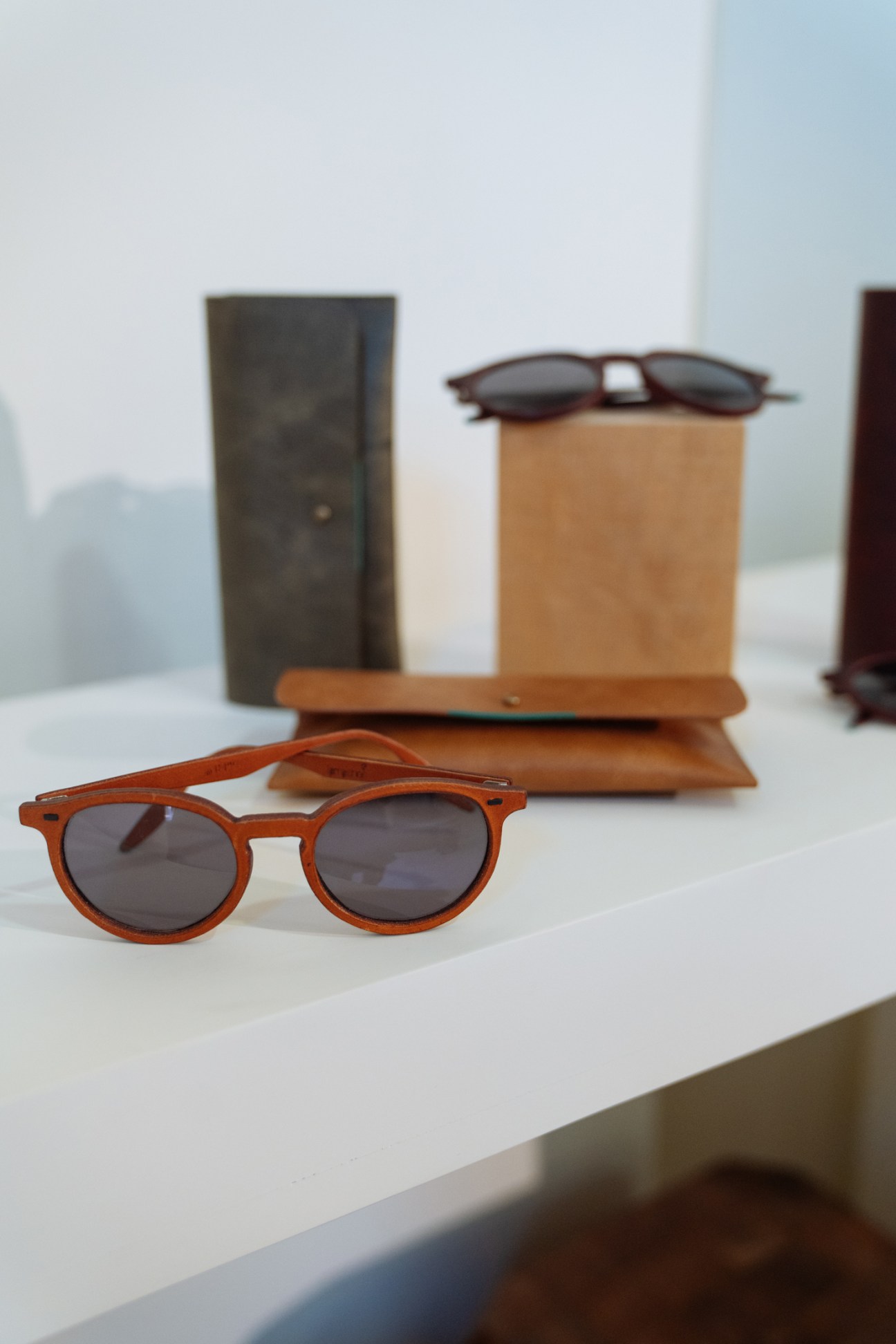 Sunglasses with leather frames displayed on white surface with leather cases in background.