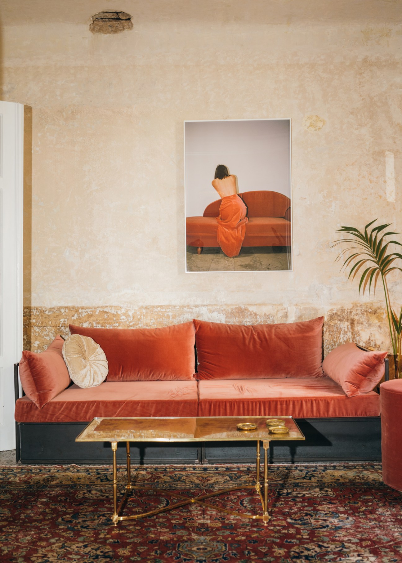 Modern living room with orange velvet sofa, framed artwork of person on couch, and ornate rug