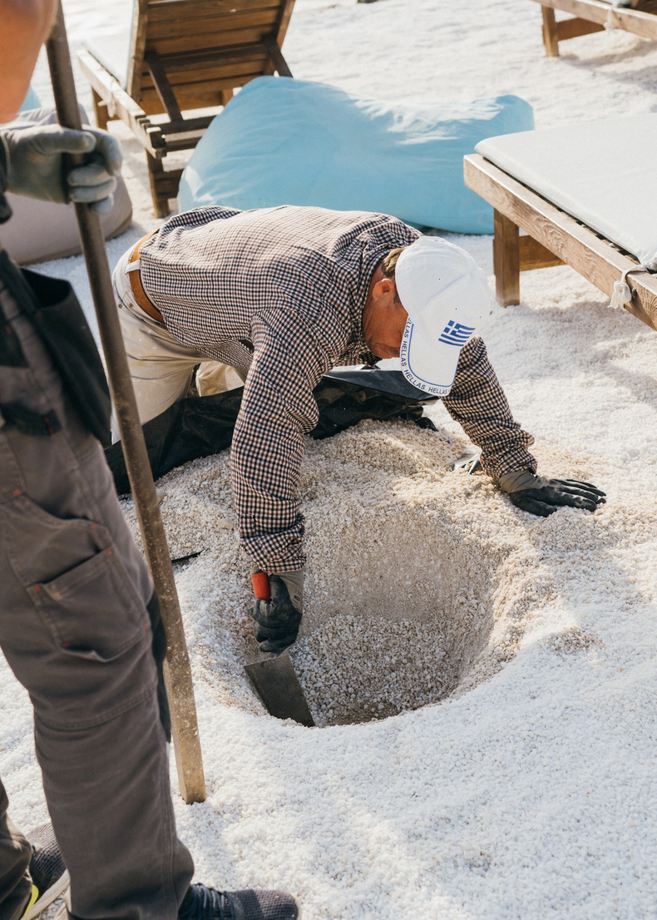 Worker smoothing sand on Makryammos beach using a shovel, preparing the beach for summer tourists.