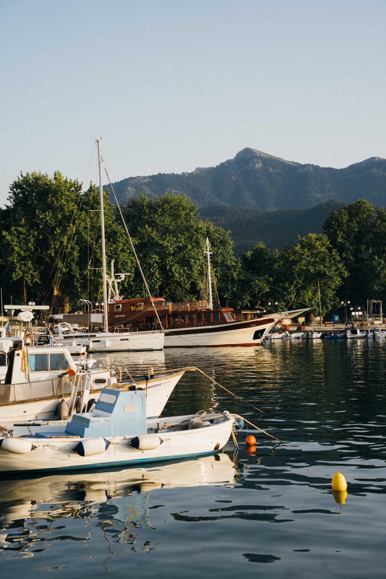 Wooden fishing boats moored at Thassos's Old Port with forested mountains in the background.