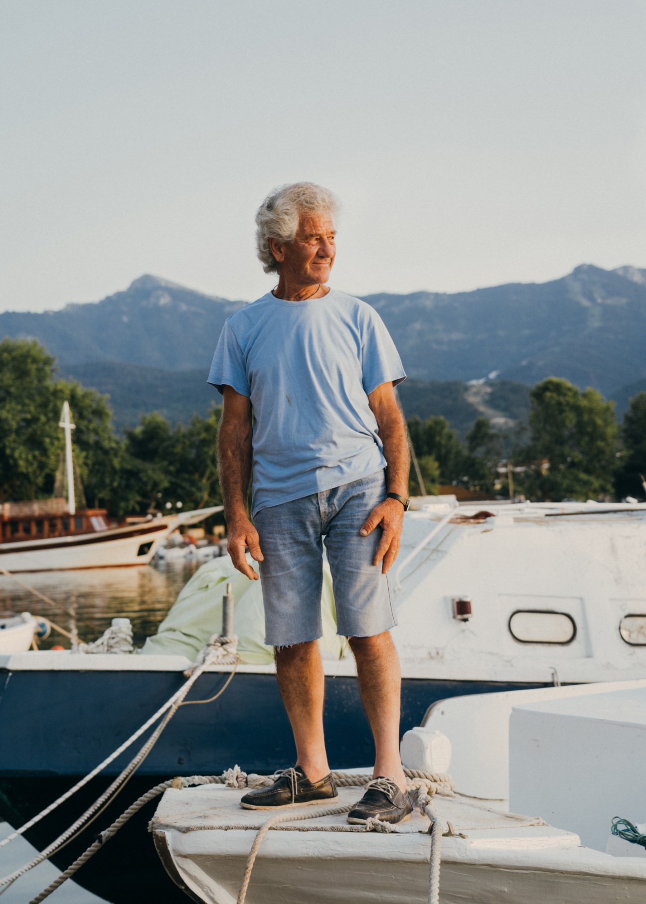 Elderly fisherman Angelos stands on his wooden boat with mountains visible in the background on Thassos island.