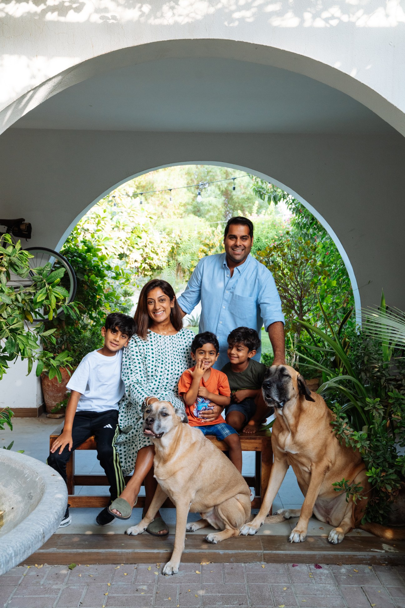 Akshay Sardana poses with his family and two dogs in their garden courtyard under a curved archway.