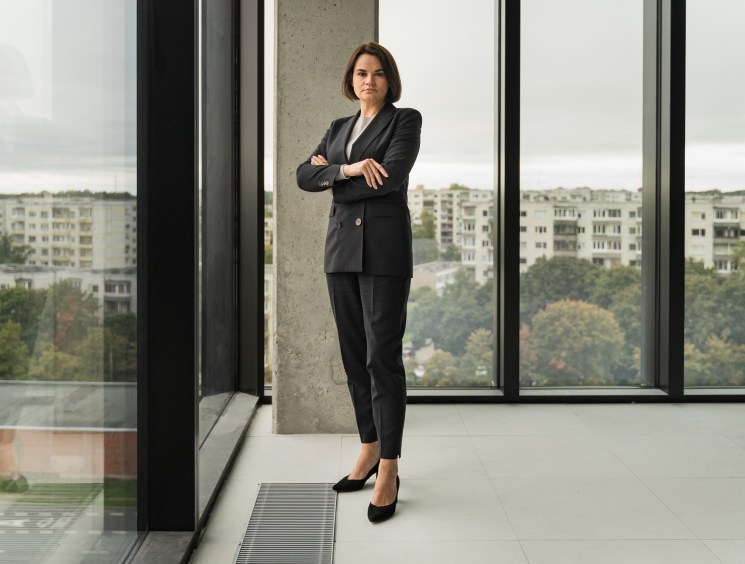 Sviatlana Tsikhanouskaya stands with crossed arms in a modern office with floor-to-ceiling windows