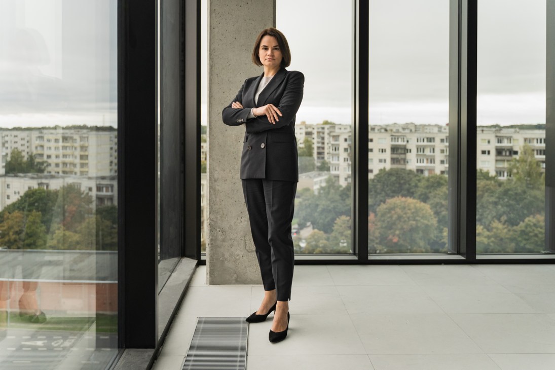Sviatlana Tsikhanouskaya stands with crossed arms in a modern office with floor-to-ceiling windows
