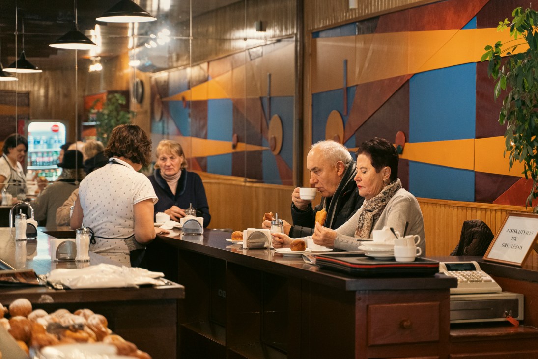 Interior of Spurgine café showing customers at counter with colorful geometric wall mural and pendant lighting
