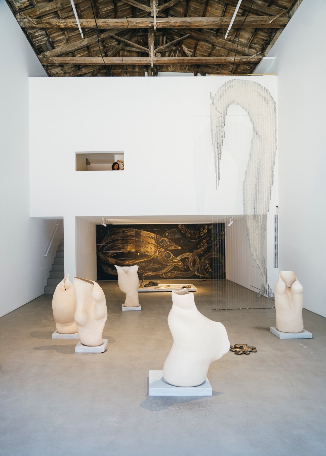 White sculptural vessels displayed on pedestals in The Intermission gallery space with exposed wooden ceiling beams