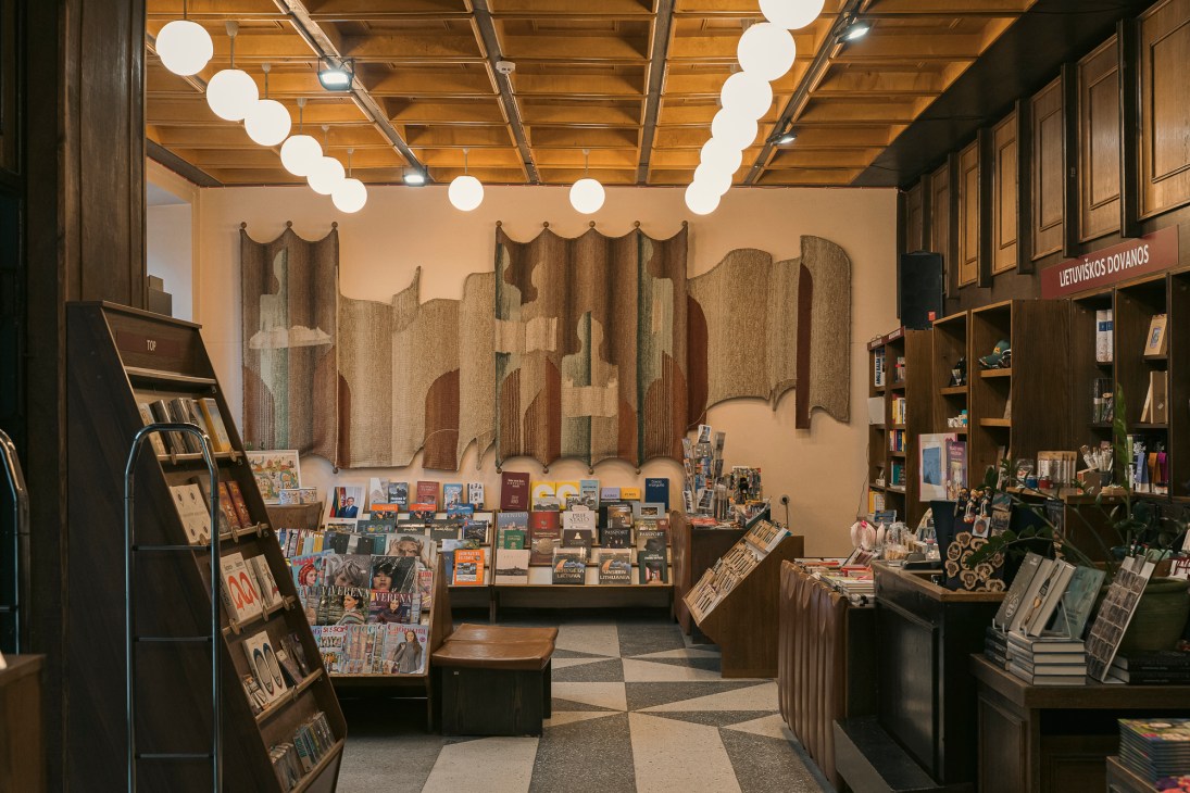 Interior of Centrinis Knygynas bookshop with wooden shelves, spherical lights, and woven wall tapestry
