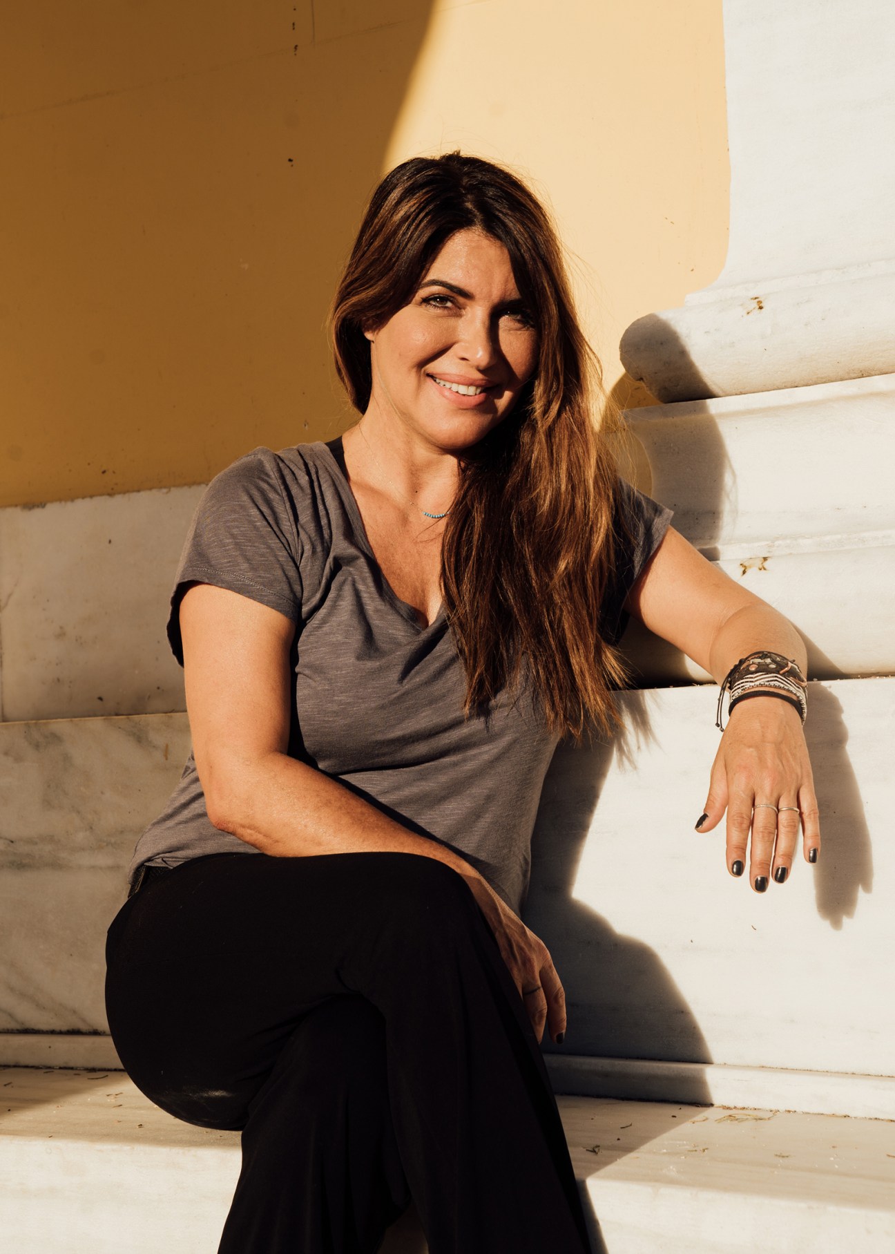 Afroditi Simiti sitting on white stone steps wearing a grey t-shirt and black pants, smiling at the camera
