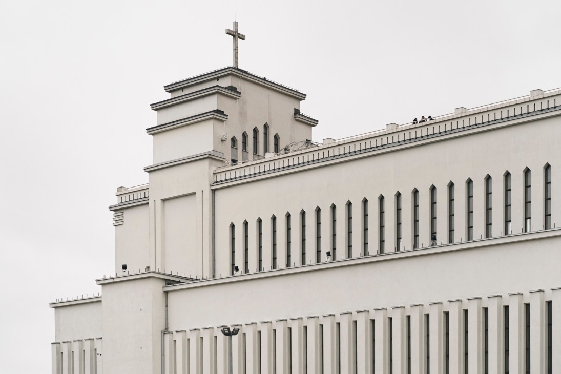 White modernist church building with tall bell tower and cross on top against overcast sky